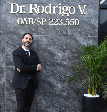 Rodrigo Vieira, advogado, em pé com os braços cruzados em frente à fachada do escritório